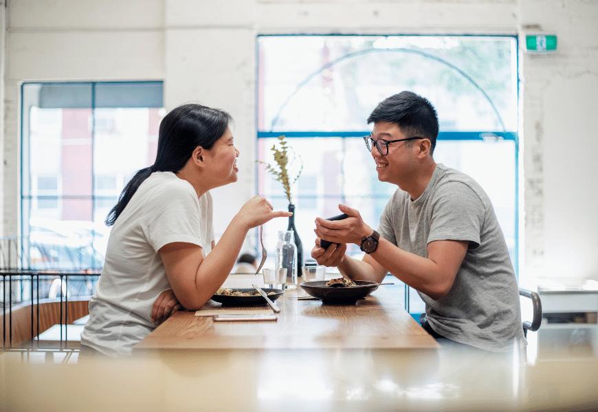 Smiling couple looking at mobile phone as they sit in a café eating a meal