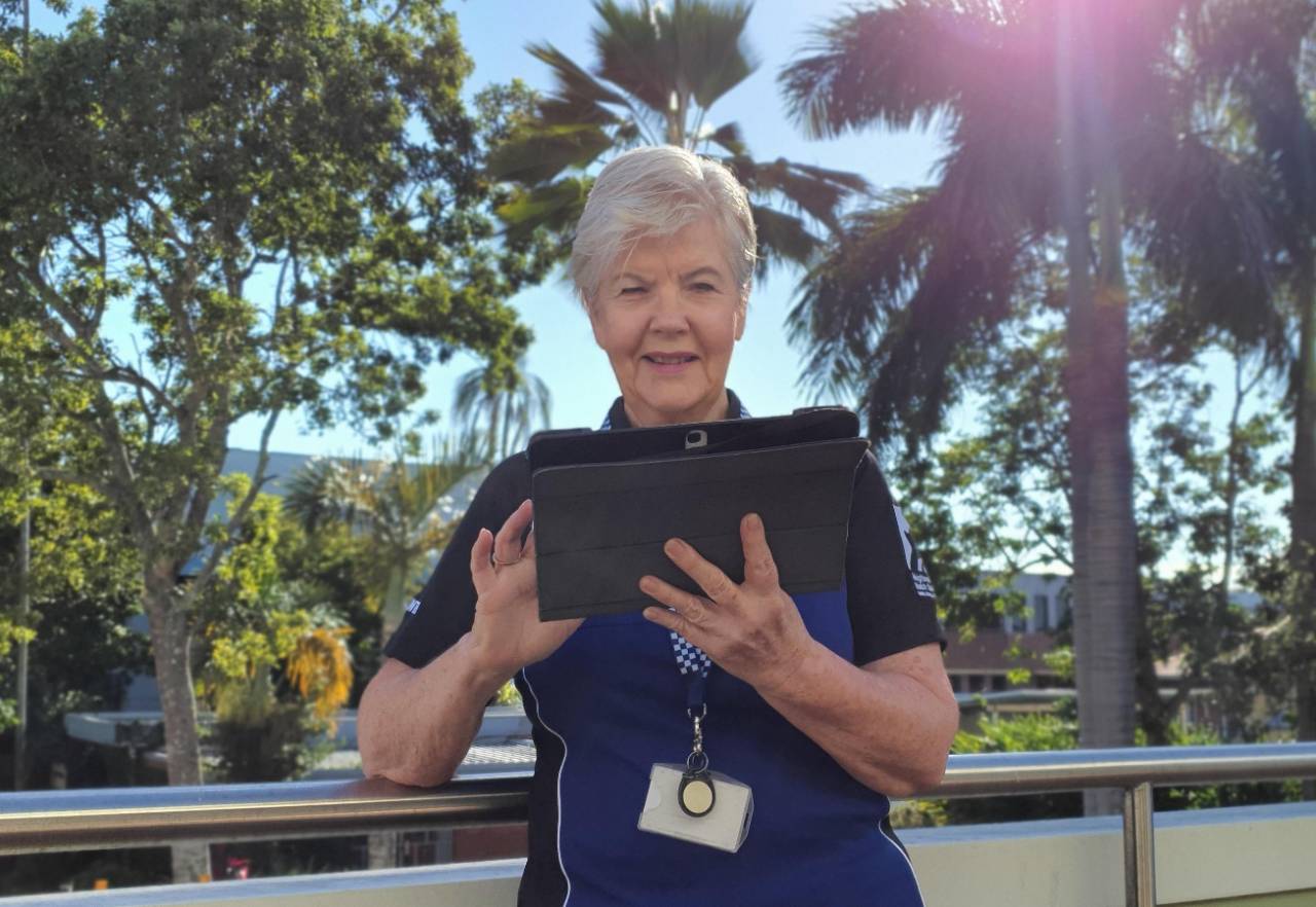 Older female wearing lanyard using tablet device on a balcony with trees in background