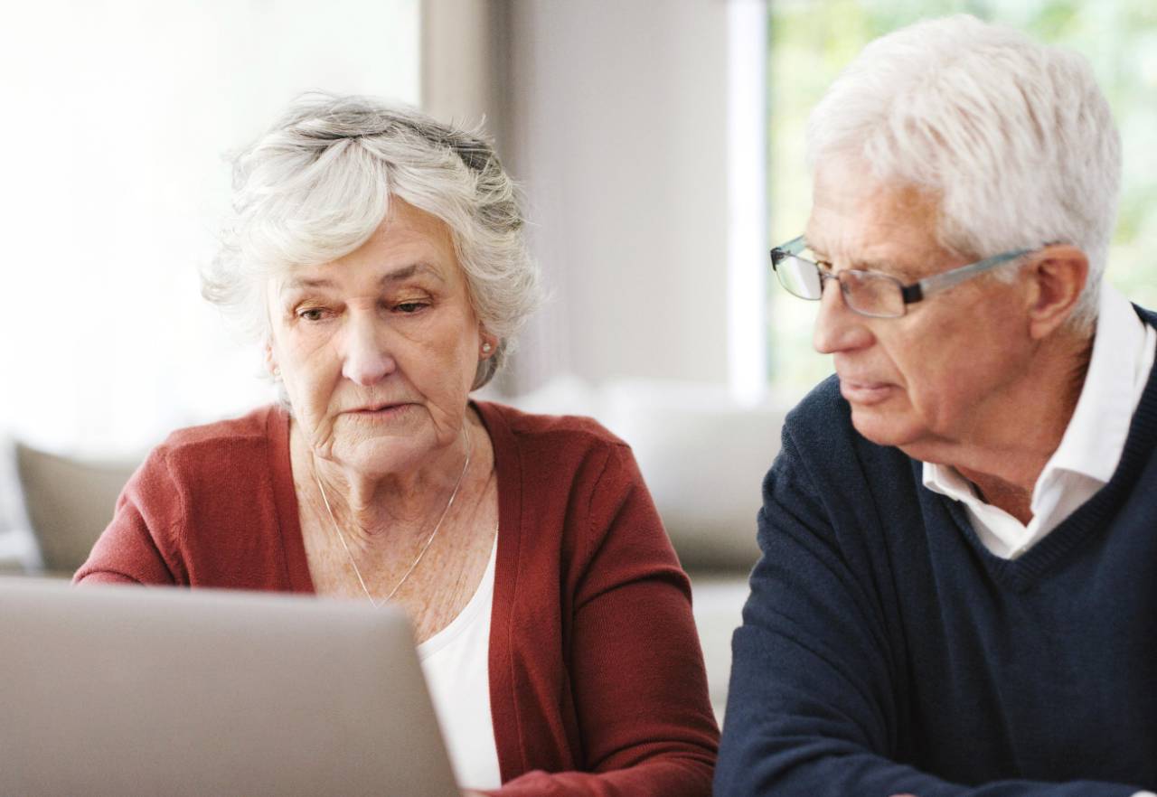 Older female and male couple looking at laptop on table in front of them